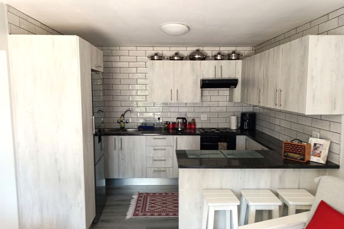 Modern kitchen featuring light wood-grain cabinetry, dark granite countertops, subway tile backsplash, and a functional breakfast bar layout.