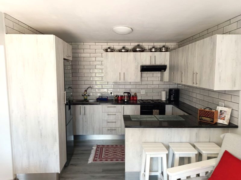 Modern kitchen featuring light wood-grain cabinetry, dark granite countertops, subway tile backsplash, and a functional breakfast bar layout.