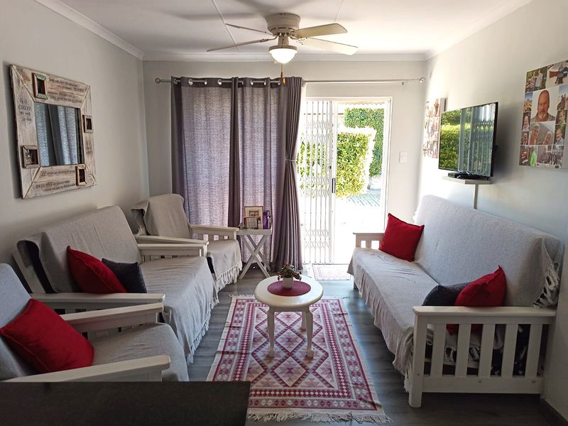 A well-maintained living room featuring laminate flooring, a ceiling fan, and a sliding glass door providing direct access to the outdoor area.