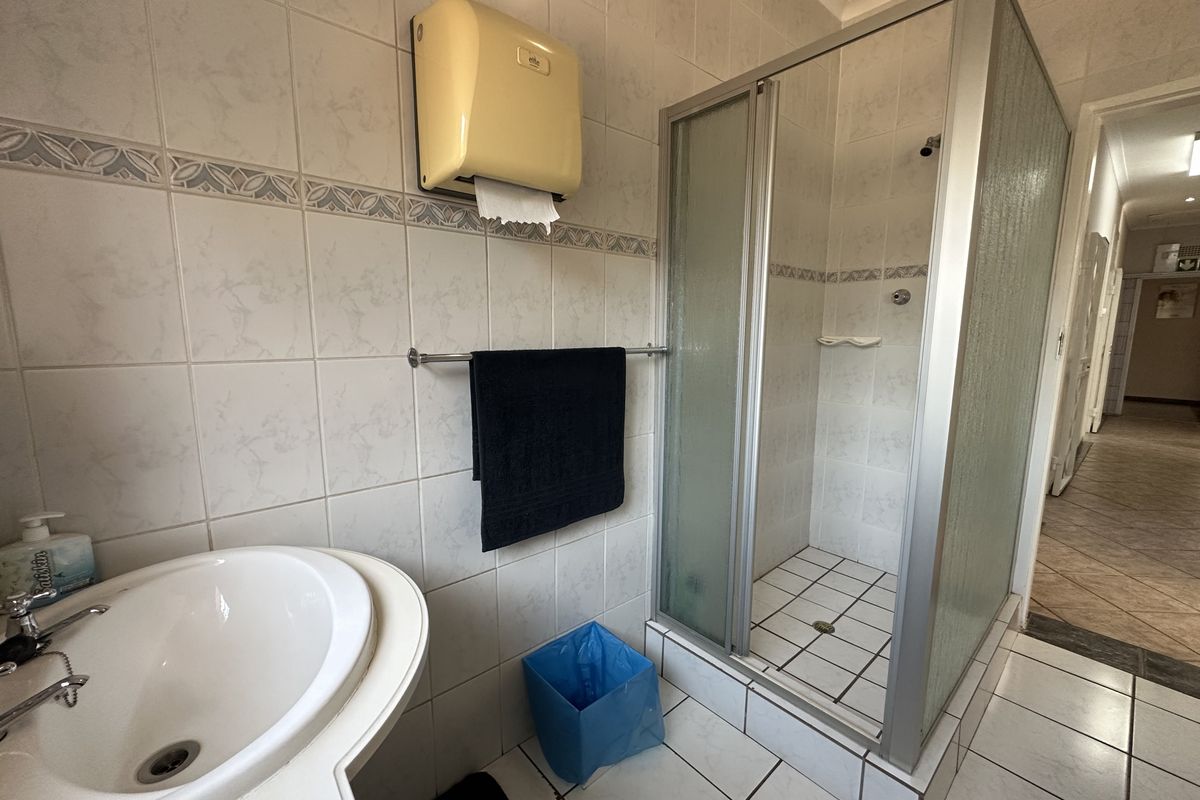 A functional bathroom featuring a shower enclosure, pedestal basin, and tiled finishes, currently showing signs of age and wear.