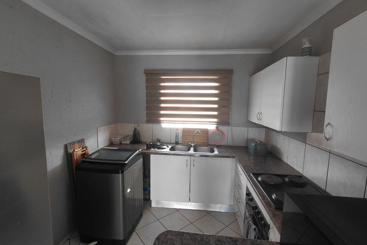 A functional kitchen featuring built-in cabinetry, laminate countertops, a double basin sink, and an integrated electric hob and oven with tiled flooring.