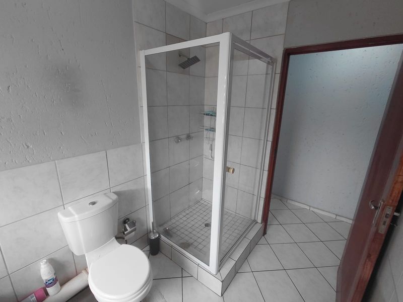 A functional bathroom featuring a glass-enclosed shower, a standard toilet, and tiled finishes throughout.