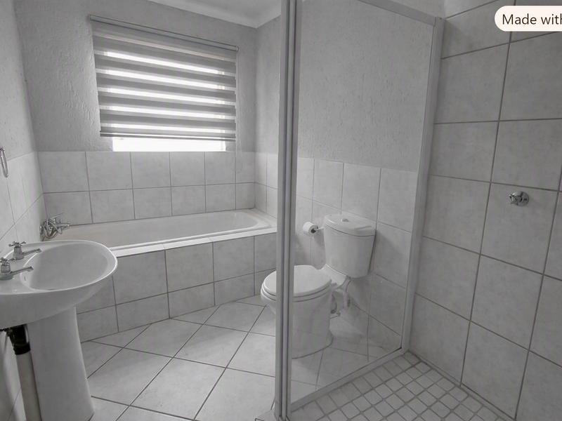A clean, functional bathroom featuring a pedestal basin, built-in bathtub, separate shower enclosure, and neutral tiled finishes throughout.