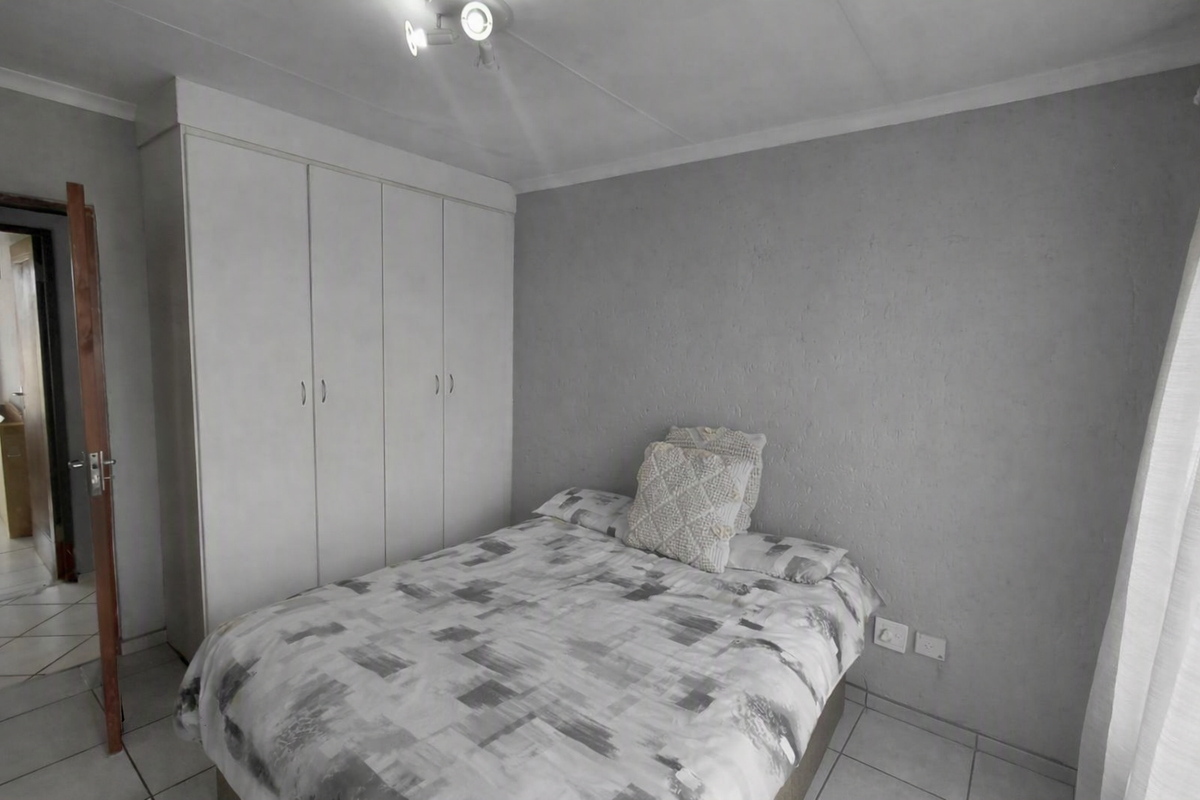 A bedroom featuring built-in cupboards, neutral grey walls, and tiled flooring, providing a functional and clean living space.