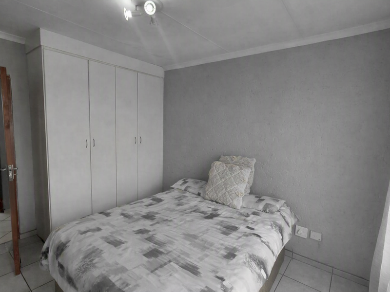 A bedroom featuring built-in cupboards, neutral grey walls, and tiled flooring, providing a functional and clean living space.