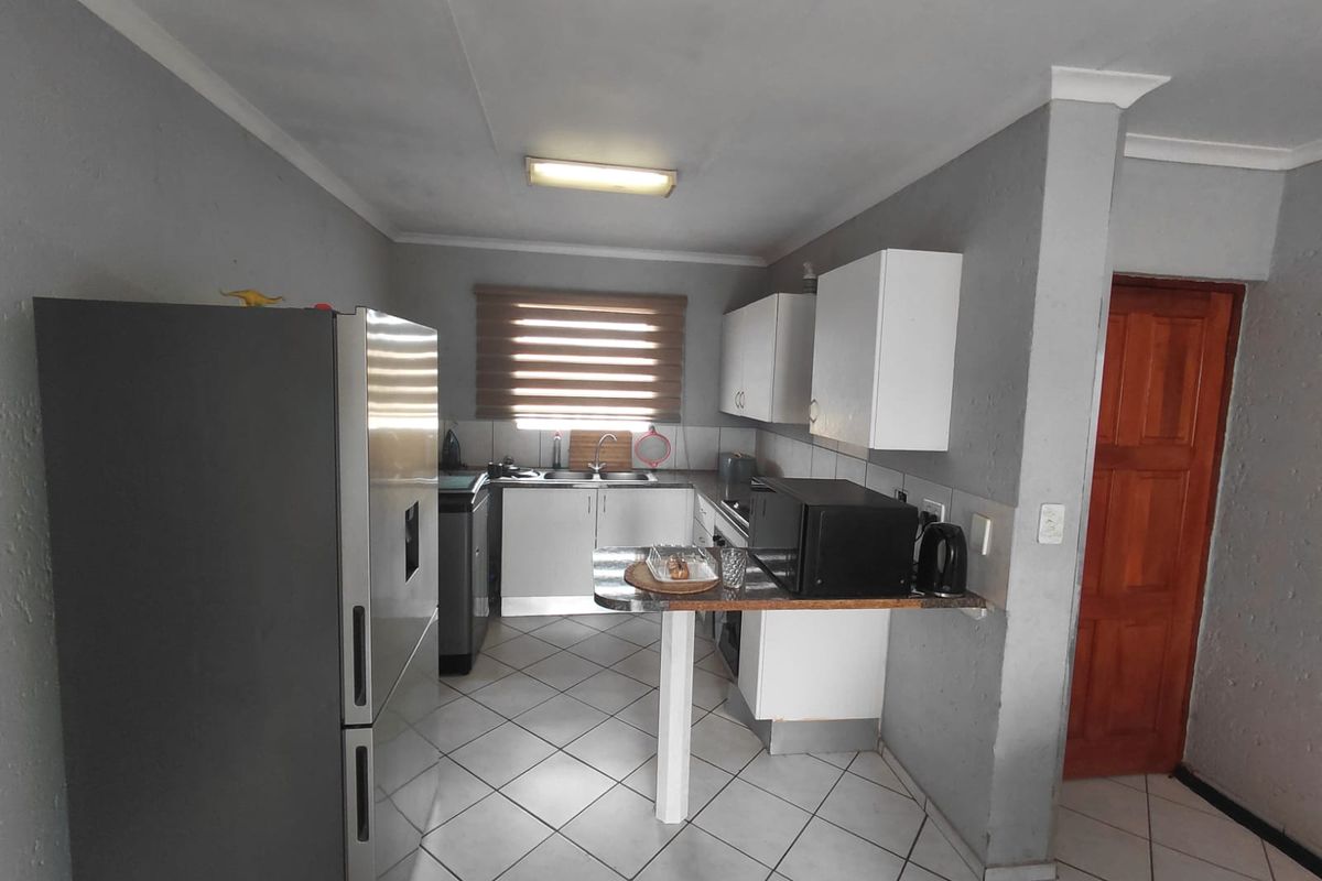 A functional kitchen featuring tiled flooring, built-in cabinetry, a breakfast bar, and a window with blinds, offering a practical layout for daily use.