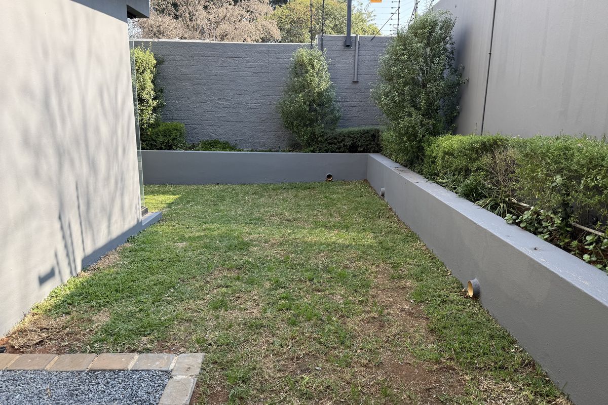 A private rear garden featuring a lawn area, raised retaining walls, and secure boundary walls with electric fencing.