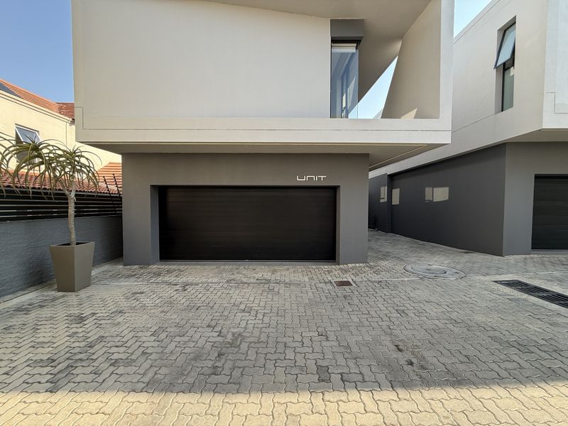 Modern townhouse exterior featuring a sleek dark automated garage door, paved driveway, and contemporary architectural design with a cantilevered upper level.