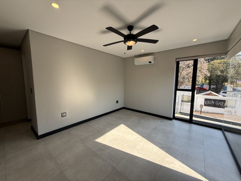 A bright, empty living area featuring modern tiled floors, a ceiling fan, split-system air conditioning, and large glass doors providing natural light.