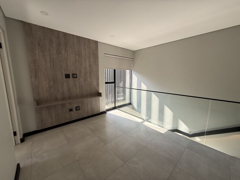A bright, modern landing or living area featuring a wood-look feature wall, glass balustrade, and neutral tiled flooring.