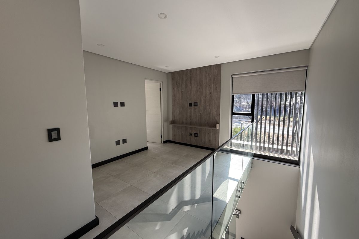 A bright, modern landing or living area featuring large format floor tiles, a timber-look feature wall with built-in shelving, and a sleek glass balustrade.
