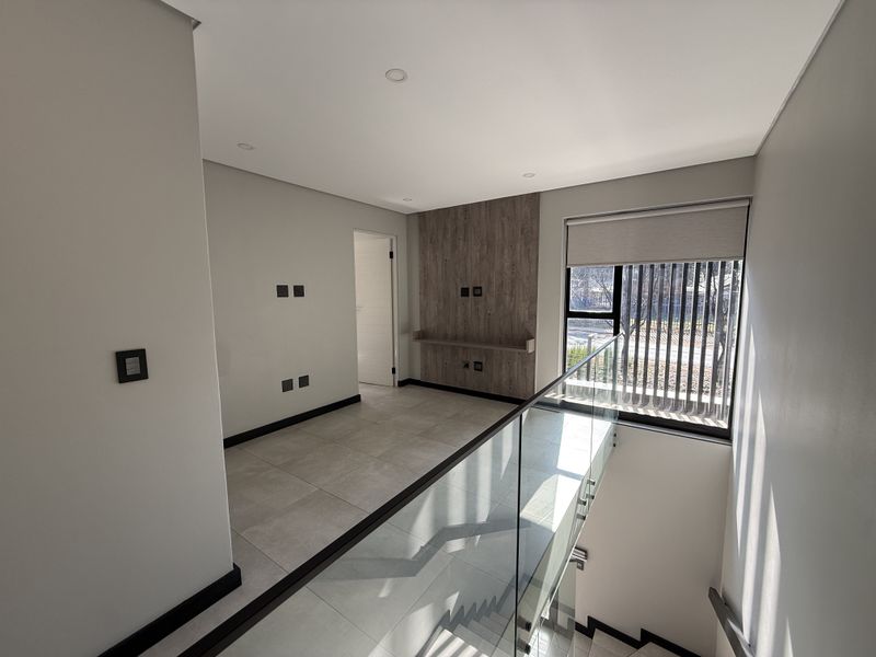 A bright, modern landing or living area featuring large format floor tiles, a timber-look feature wall with built-in shelving, and a sleek glass balustrade.
