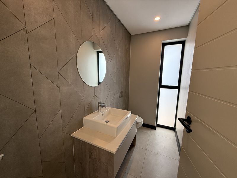 Modern guest bathroom featuring a stylish geometric tiled feature wall, vessel sink vanity, and a frosted glass window for natural light.