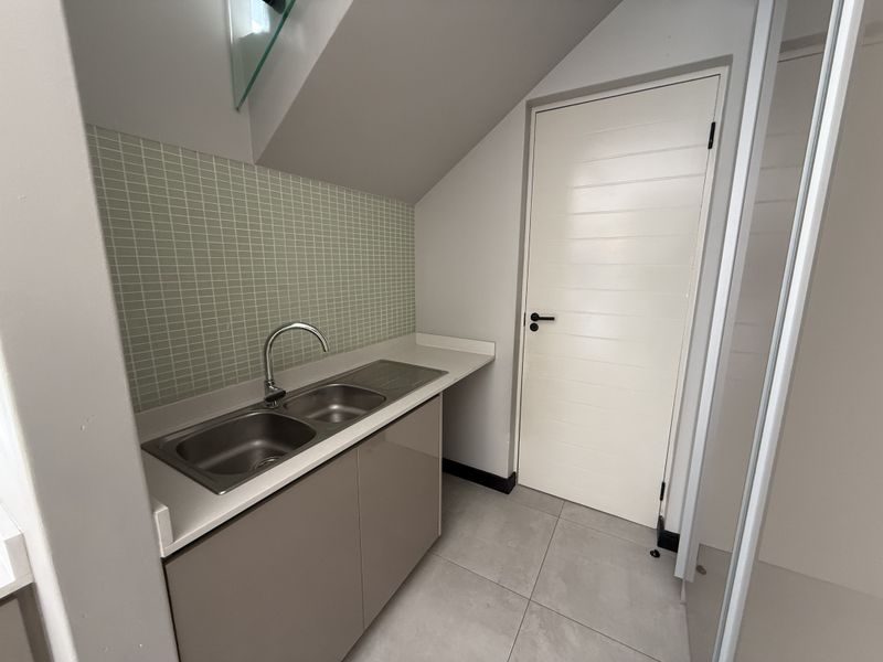 A clean and functional scullery area featuring a double sink, modern tiled splashback, and neutral cabinetry under a sloped ceiling.