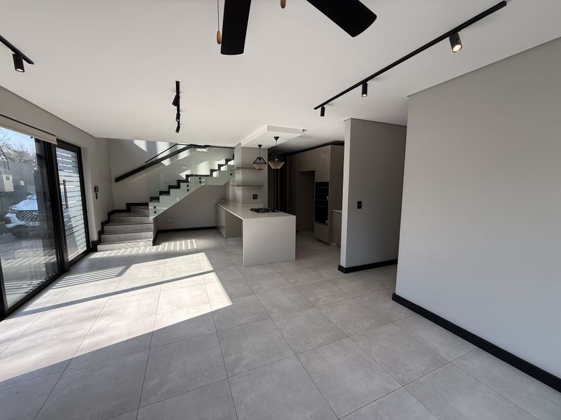 Modern open-plan living area featuring a sleek kitchen with island, built-in appliances, and a contemporary staircase with glass balustrades and large sliding doors.