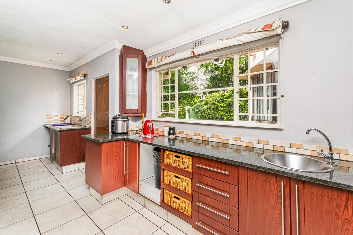 A functional kitchen featuring granite countertops, laminate cabinetry, tiled flooring, and a large window with security bars overlooking the garden.