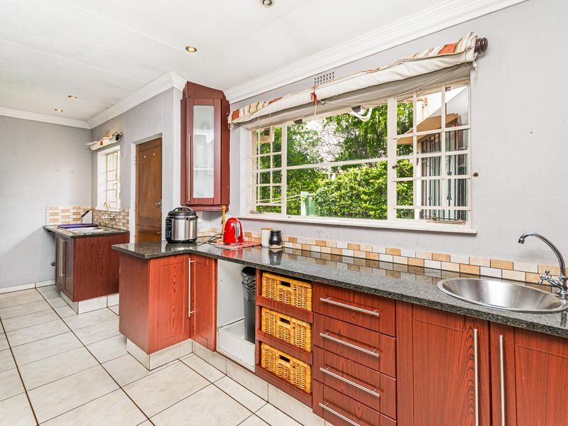 A functional kitchen featuring granite countertops, laminate cabinetry, tiled flooring, and a large window with security bars overlooking the garden.