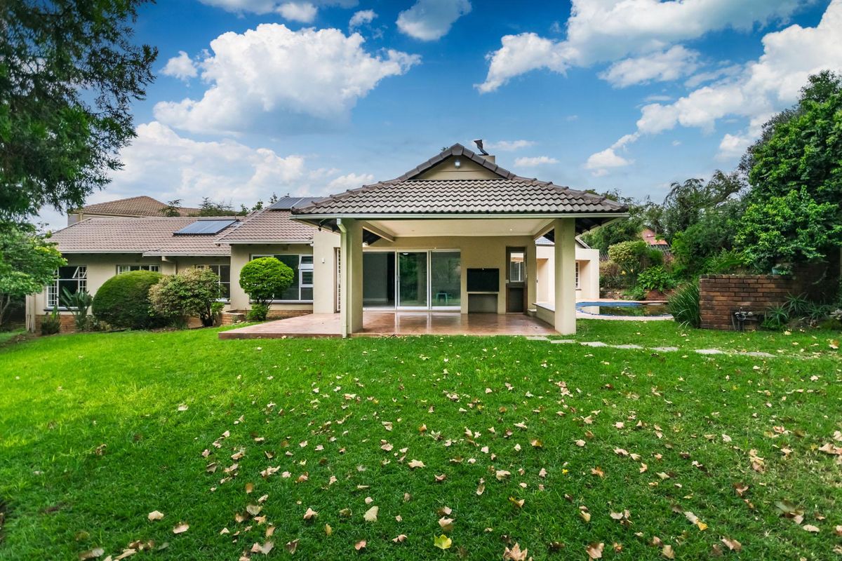 Rear view of the house featuring a spacious covered patio, sliding glass doors, solar panels, and a well-maintained garden with a swimming pool.
