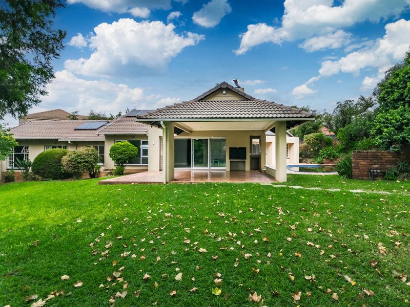 Rear view of the house featuring a spacious covered patio, sliding glass doors, solar panels, and a well-maintained garden with a swimming pool.