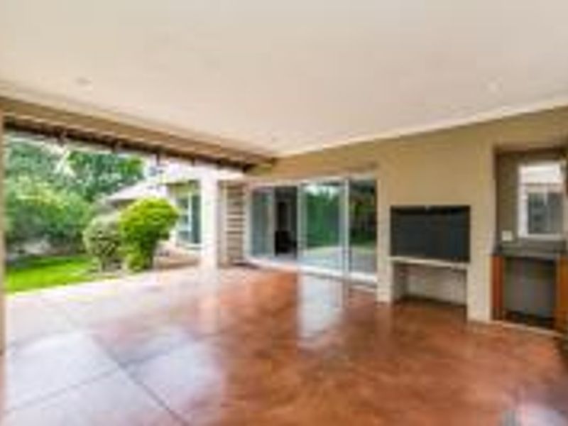 Spacious covered patio featuring polished concrete floors, a built-in braai, and seamless access to the garden through large sliding glass doors.