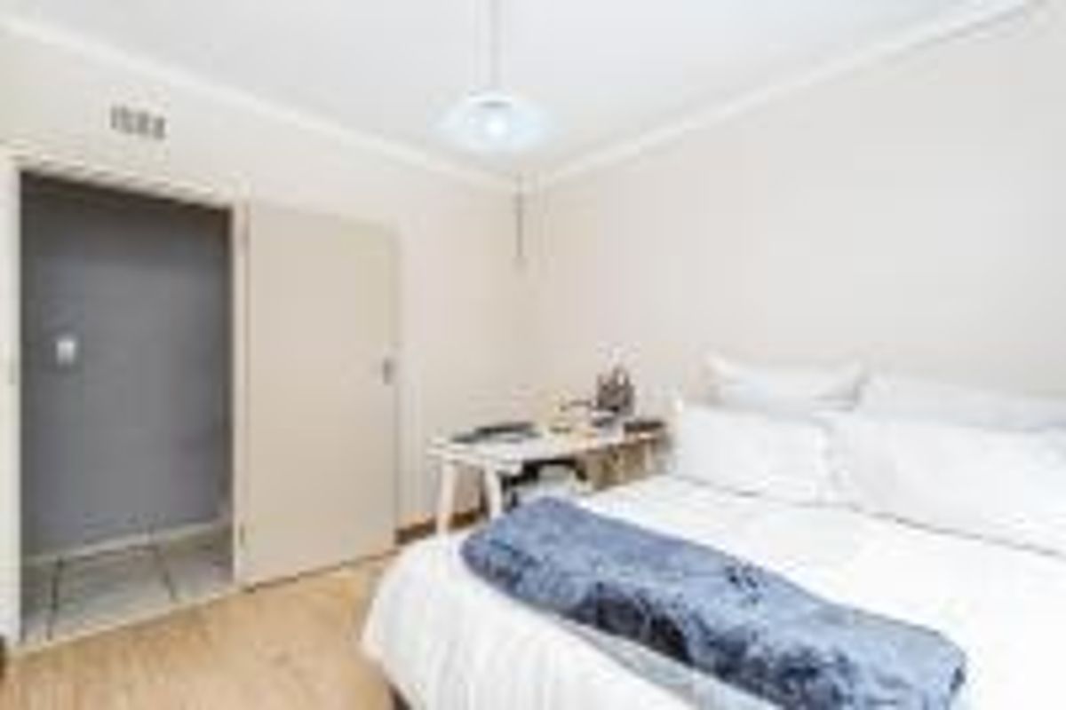 A functional bedroom featuring laminate flooring, cove cornicing, and a neutral color palette, providing a comfortable and well-lit sleeping space.