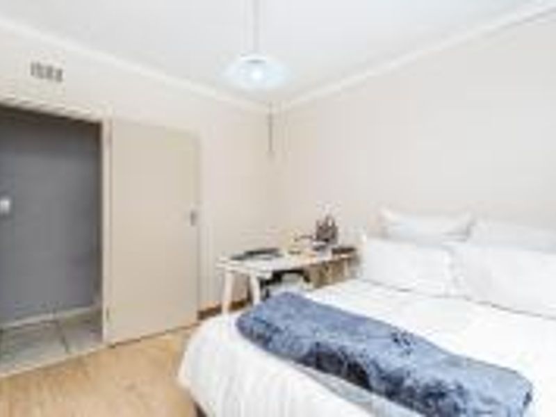 A functional bedroom featuring laminate flooring, cove cornicing, and a neutral color palette, providing a comfortable and well-lit sleeping space.