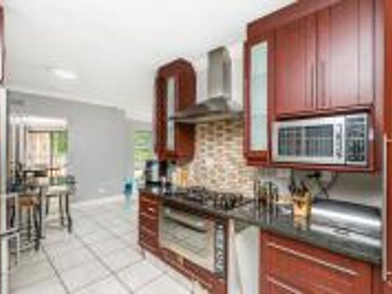 A functional kitchen featuring cherry wood cabinetry, granite countertops, a mosaic tile backsplash, and integrated stainless steel appliances including a gas hob and oven.