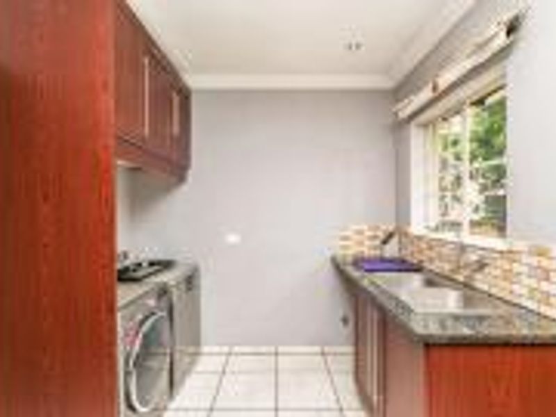 A functional laundry room featuring built-in wooden cabinetry, granite countertops, a double sink, and tiled backsplash with neutral floor tiles.