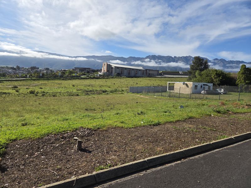 A vacant residential plot featuring open grass land, perimeter fencing, and scenic mountain views in the background.