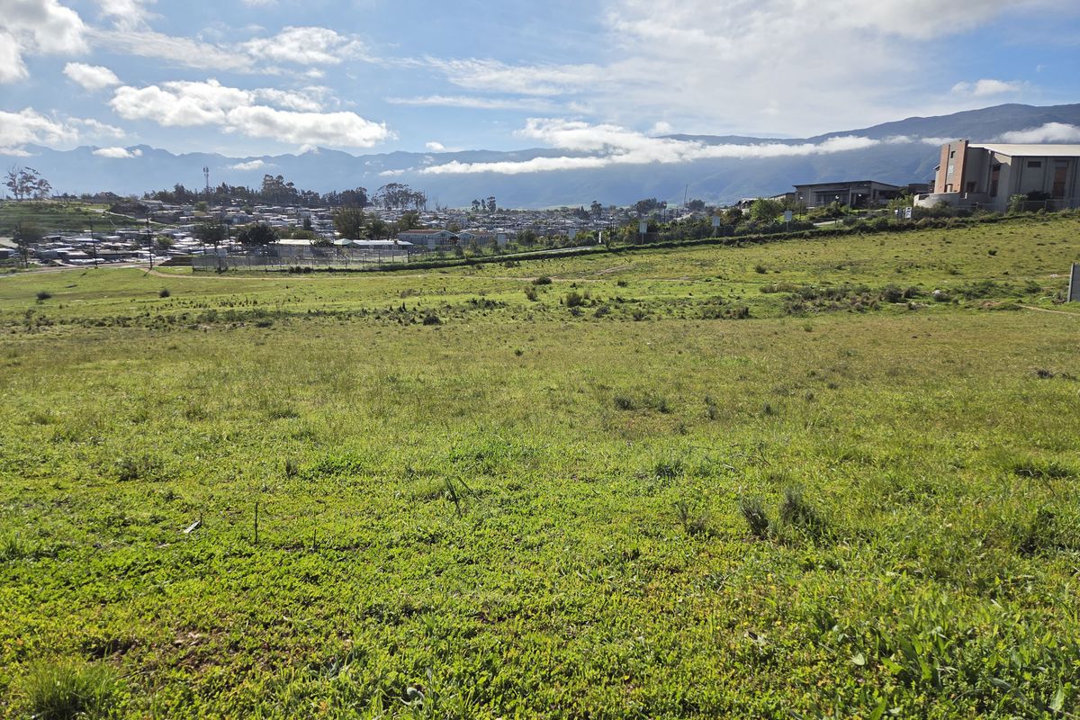 A wide-angle view of a vacant residential plot featuring natural grassland with scenic mountain views in the background.
