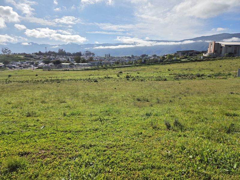 A wide-angle view of a vacant residential plot featuring natural grassland with scenic mountain views in the background.