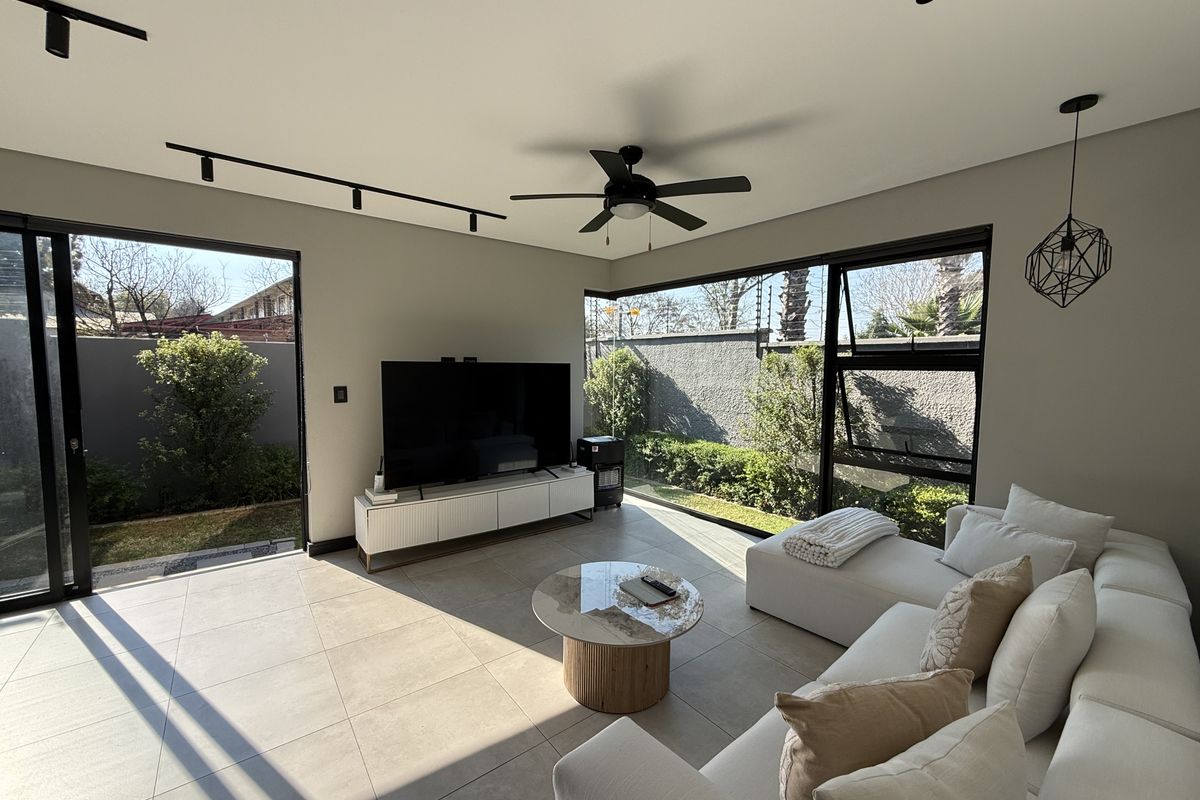 Modern living room featuring large format floor tiles, black aluminium sliding doors, and expansive windows providing seamless indoor-outdoor flow to the garden.