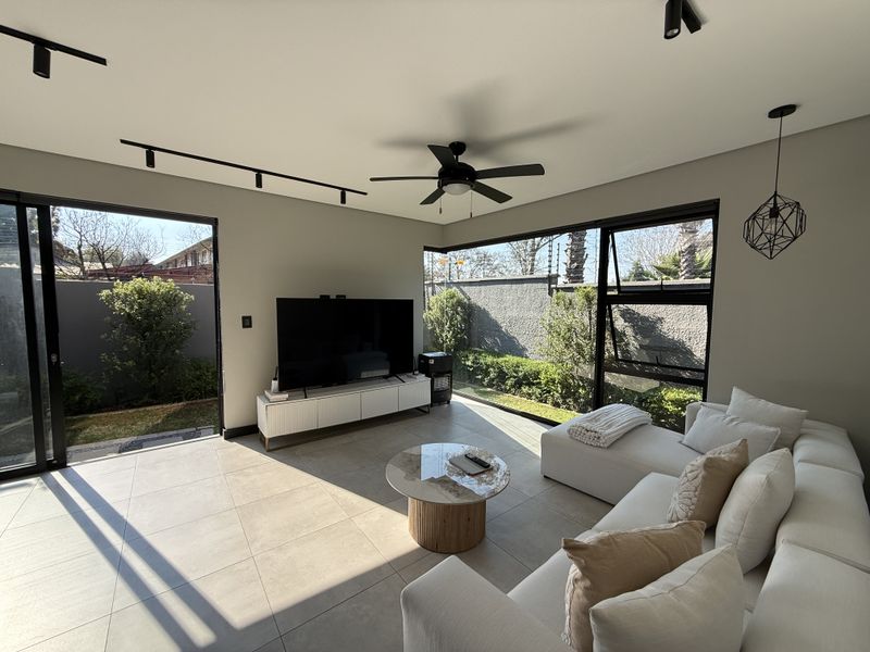 Modern living room featuring large format floor tiles, black aluminium sliding doors, and expansive windows providing seamless indoor-outdoor flow to the garden.