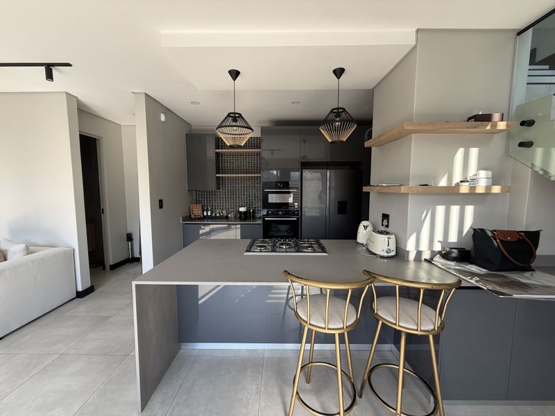 Modern open-plan kitchen featuring dark grey cabinetry, stone countertops, a central gas hob island, and stylish floating timber shelving.