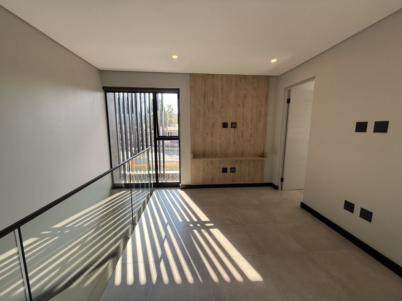 Modern, bright living area featuring tiled floors, a wood-look feature wall with built-in shelving, and a sleek glass balustrade overlooking the lower level.