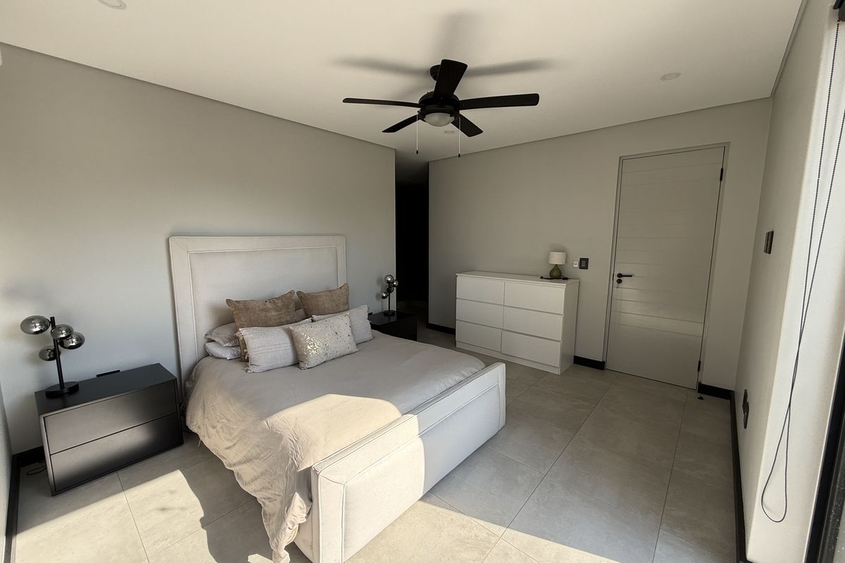 A modern, well-maintained bedroom featuring neutral wall tones, large format floor tiles, a ceiling fan, and recessed lighting.