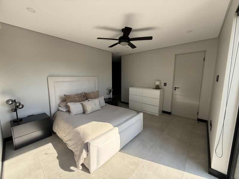 A modern, well-maintained bedroom featuring neutral wall tones, large format floor tiles, a ceiling fan, and recessed lighting.