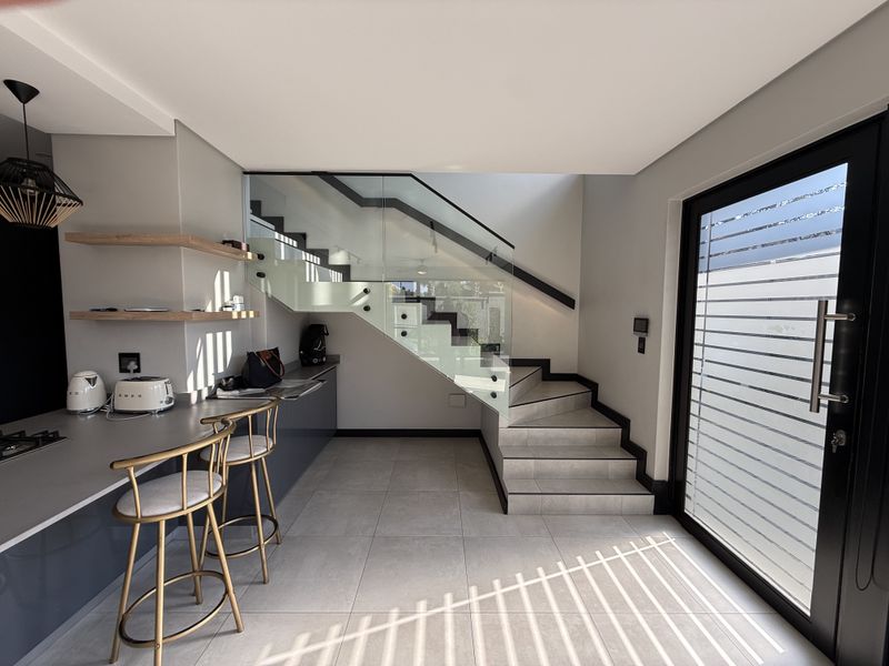 Modern open-plan kitchen area featuring sleek cabinetry, stone countertops, a gas hob, and a contemporary staircase with a glass balustrade.