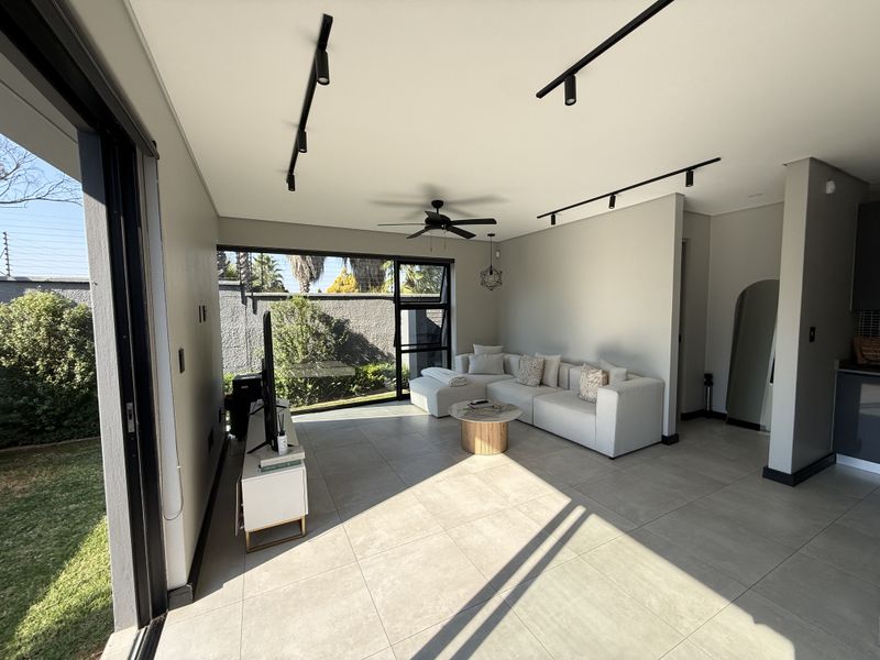 Modern open-plan living area featuring large sliding glass doors, contemporary track lighting, a ceiling fan, and neutral tiled flooring with direct garden access.