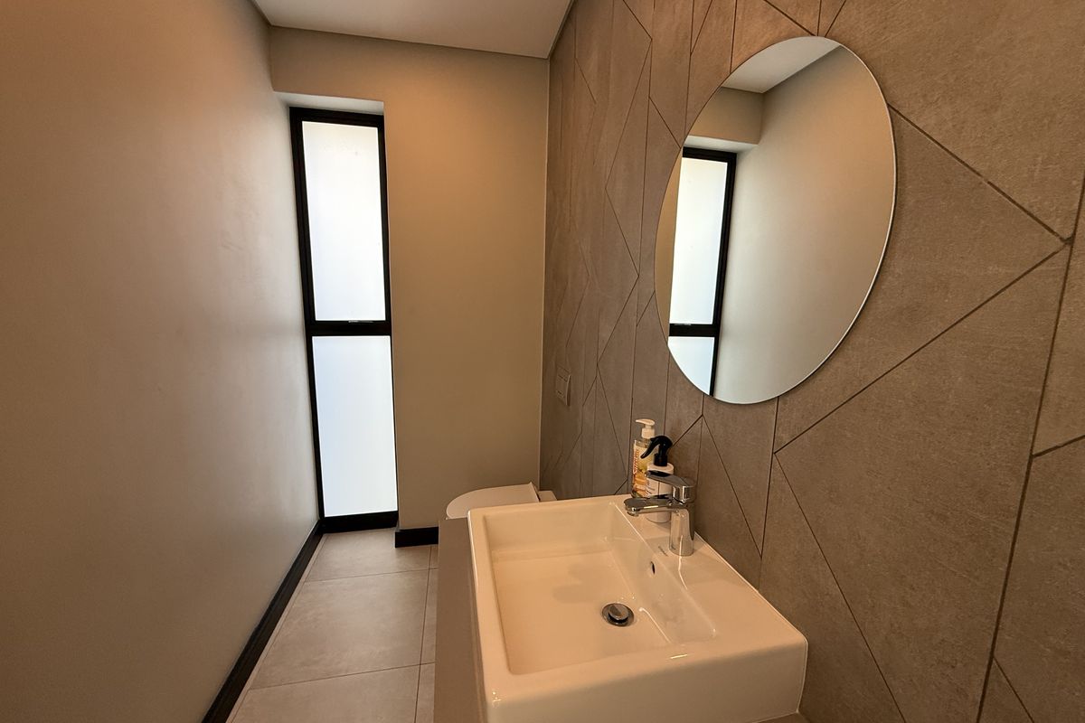 Modern guest bathroom featuring a wall-mounted basin, chrome mixer tap, and a stylish geometric tiled feature wall with neutral floor tiles.