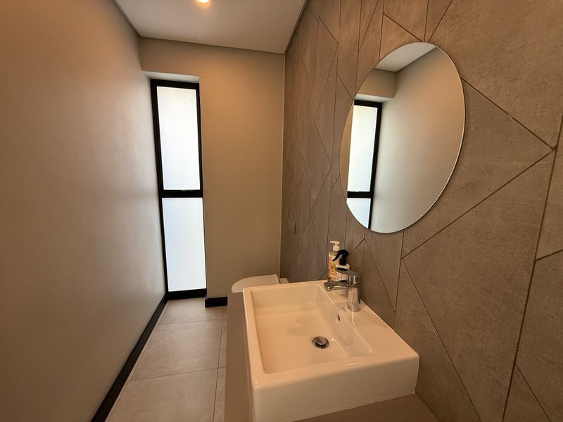 Modern guest bathroom featuring a wall-mounted basin, chrome mixer tap, and a stylish geometric tiled feature wall with neutral floor tiles.