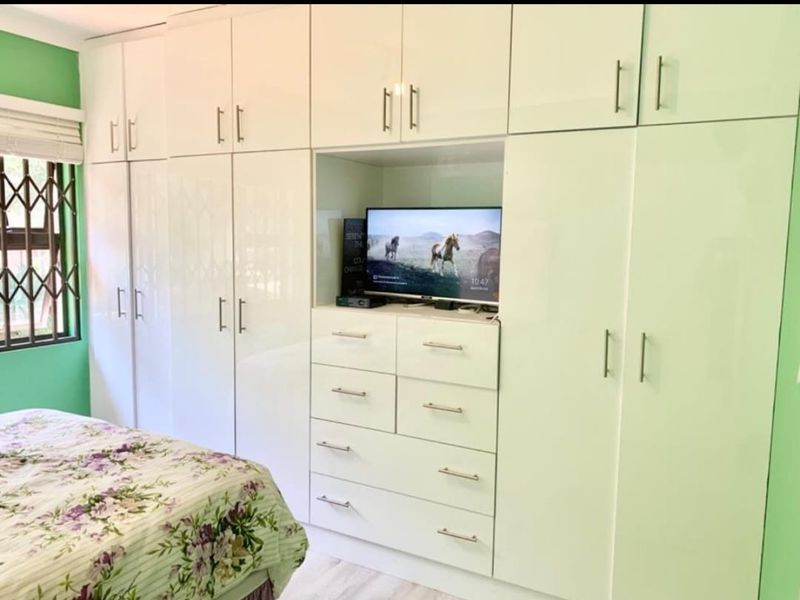 A bedroom featuring extensive white built-in cabinetry with integrated storage and a dedicated media alcove, complemented by a security gate on the window.