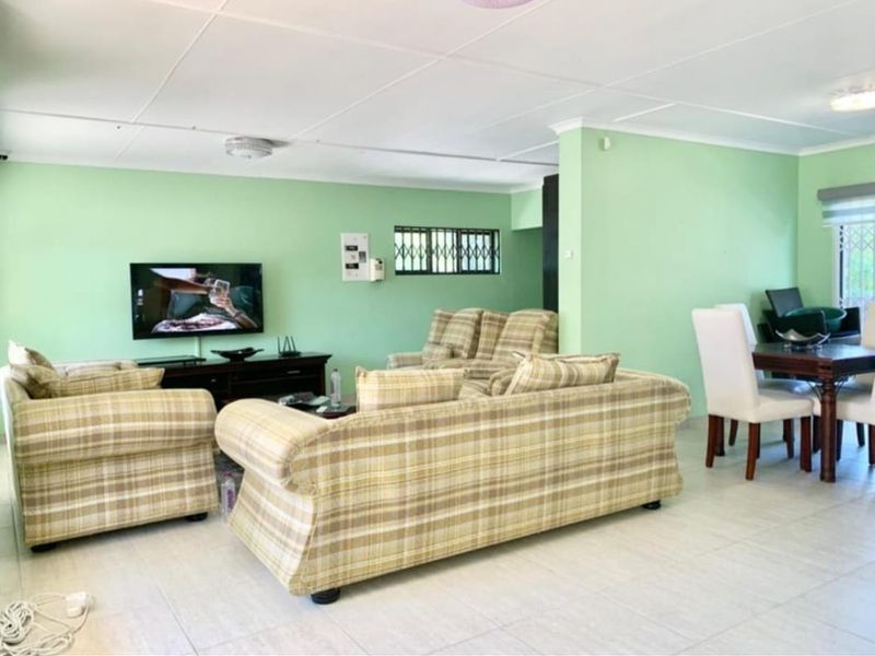 An open-plan living and dining area featuring tiled flooring and neutral green walls, offering a functional layout for family living.