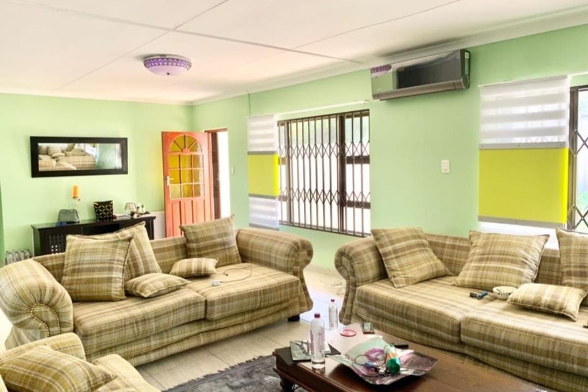 A spacious living room featuring tiled flooring, security bars on windows, and a wall-mounted split-system air conditioner.