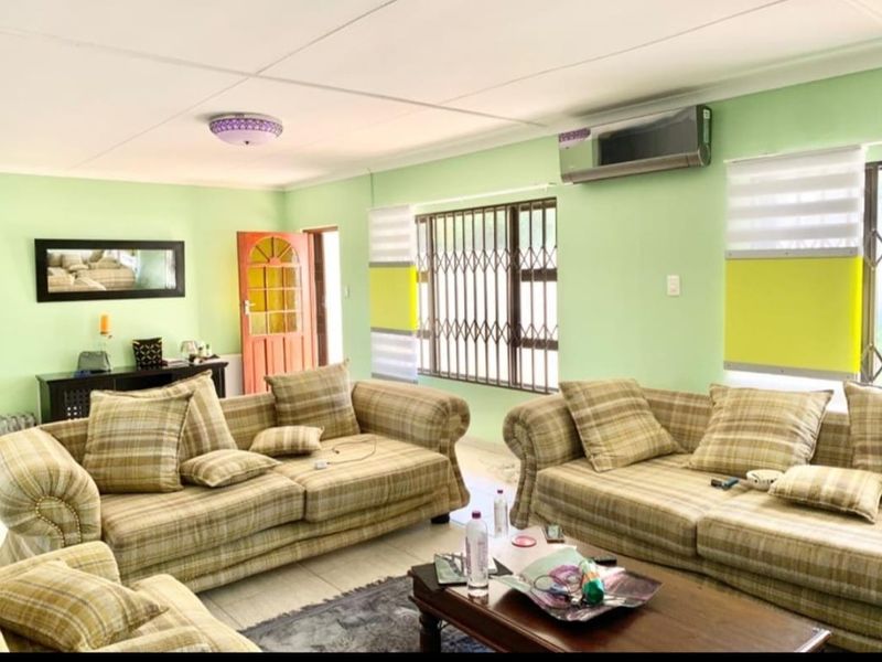 A spacious living room featuring tiled flooring, security bars on windows, and a wall-mounted split-system air conditioner.