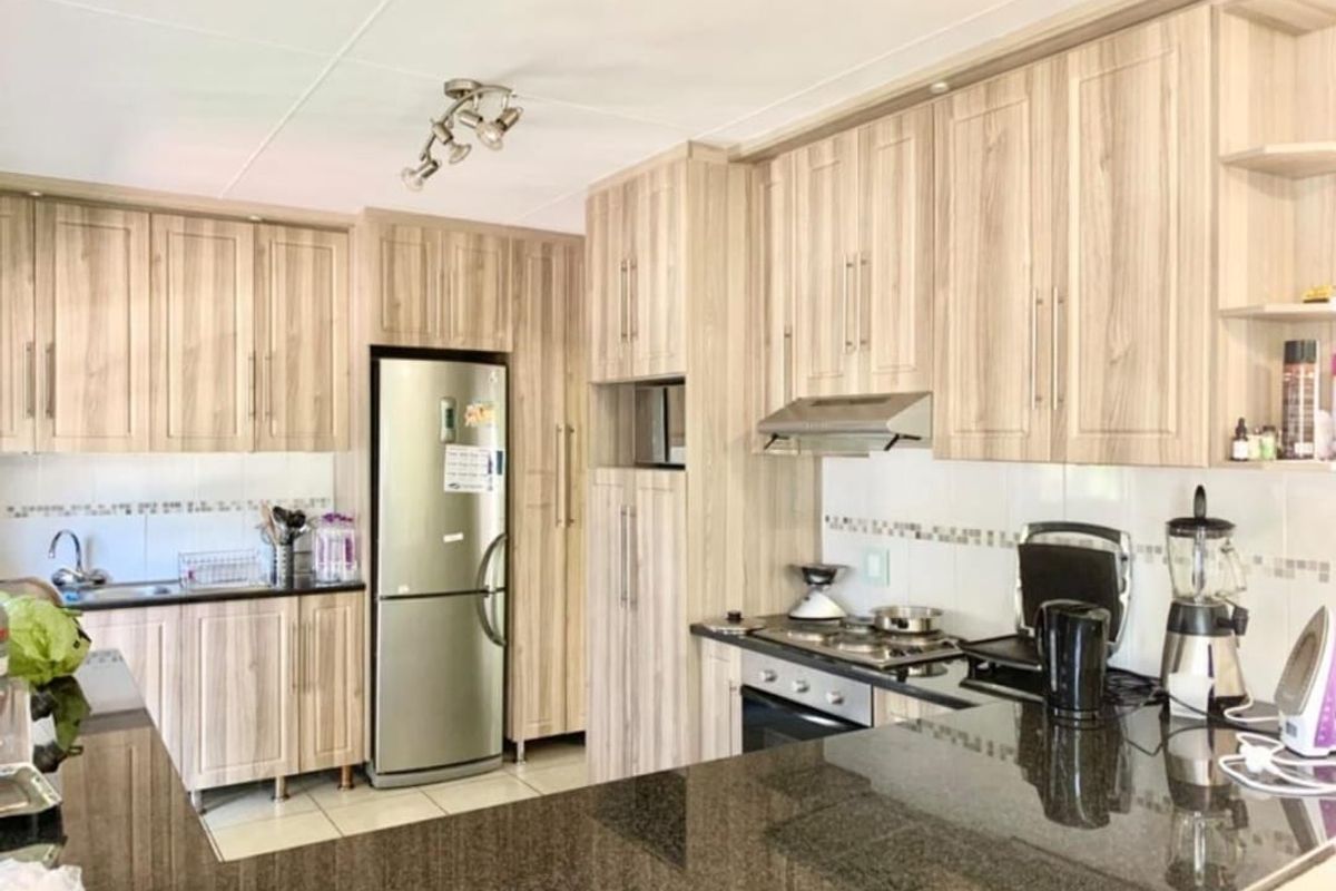 A functional kitchen featuring light wood-grain laminate cabinetry, dark granite countertops, a built-in oven, gas hob, and tiled finishes throughout.