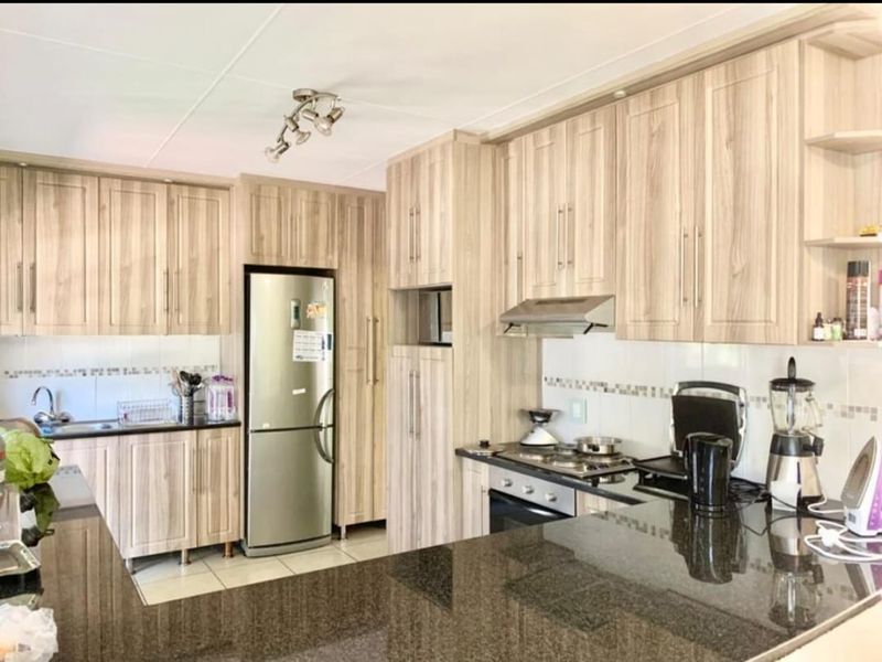 A functional kitchen featuring light wood-grain laminate cabinetry, dark granite countertops, a built-in oven, gas hob, and tiled finishes throughout.