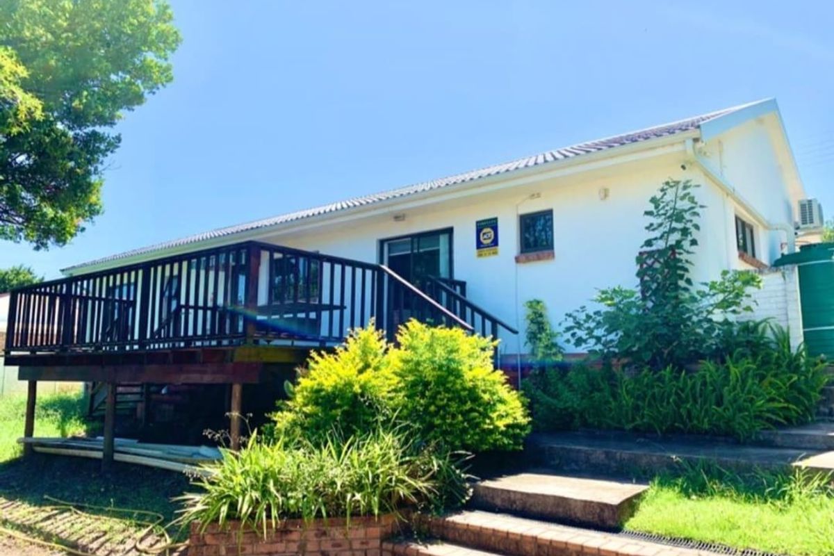 Rear exterior view of the house featuring a raised timber deck, brick staircase, and a water tank set against a landscaped garden.