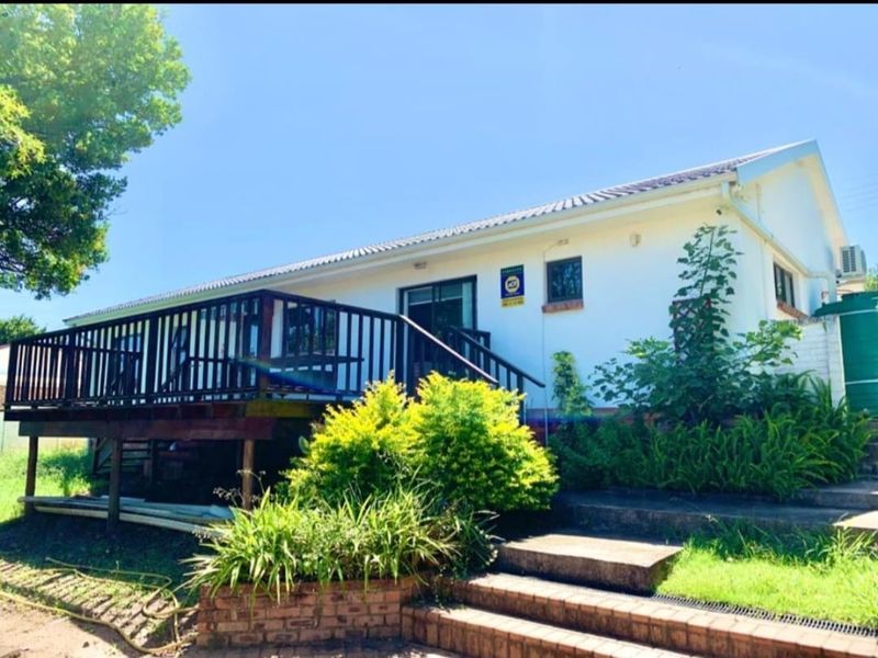 Rear exterior view of the house featuring a raised timber deck, brick staircase, and a water tank set against a landscaped garden.
