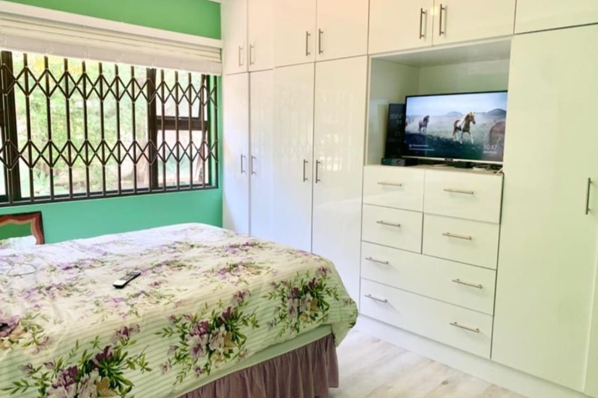 A bedroom featuring extensive white built-in cabinetry, laminate flooring, and a window fitted with a security gate.